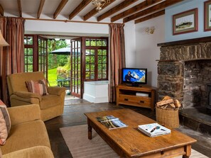 A cozy living room with a wooden sofa, a television, a fireplace, and a view of the outdoors. - 3 Bed in Llangadog (oc-bn223) (Llangadog)