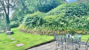 A patio with outdoor furniture, a stone wall, and lush greenery. - 3 Bed in Llangadog (oc-bn223) (Llangadog)