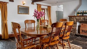 A dining room with a round wooden table, six chairs, a vase of flowers, a ceiling fan, and a stone fireplace. - 3 Bed in Llangadog (oc-bn223) (Llangadog)
