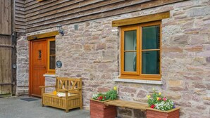 A stone building with a wooden door, a bench, and two flower planters. - 5 Bed in Brecon (oc-bn358) (Llyswen)