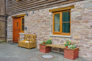 Ein Gebäude aus Stein mit einer Holztür, einer Bank und zwei Blumenkästen.