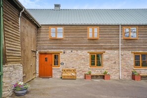 Ein zweistöckiges Holzhaus mit Steinverkleidung, einer Holztür und einer Bank mit Blumentöpfen.