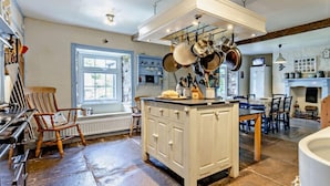 A kitchen with a central island, hanging pots, a stone floor, and a rustic aesthetic. - 9 Bed in Brecon (oc-bn222) (Sennybridge)