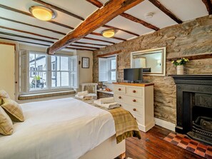 Une chambre à coucher comprenant un lit, une commode, un téléviseur, un mur en pierre, une cheminée et de grandes fenêtres.