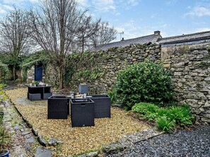 Eine Steinsäule, Sitzgelegenheiten im Freien und ein Gartenbereich.