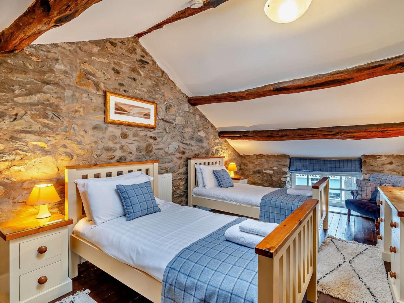 Une chambre avec deux lits, des murs en pierre, des poutres en bois, un tableau au mur et une fenêtre.