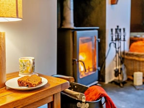 A cozy room with a wooden table, a plate of bread, a mug, a fireplace, and a wicker basket. - 5 Bed in Cartmel (oc-80332) (Cartmel)