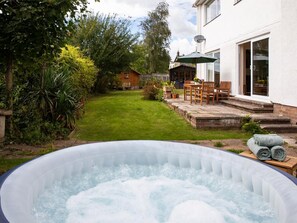 Ein Whirlpool in einem Garten mit Rasen, einer Holzterrasse und einem Haus mit Satellitenschüssel.