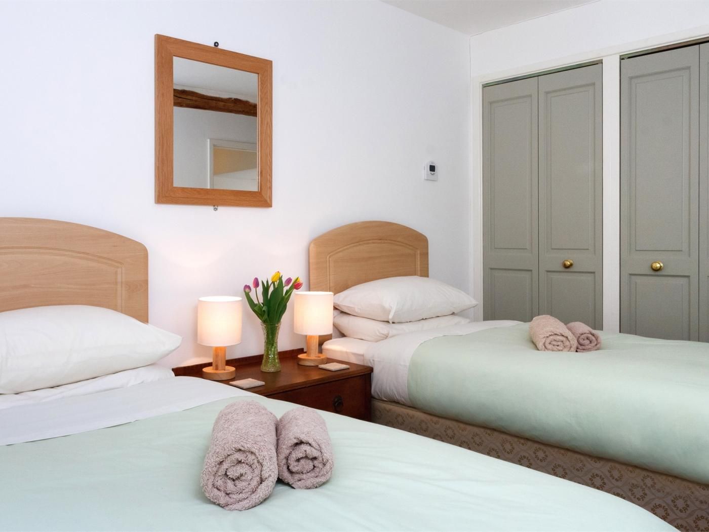 Habitación de hotel con dos camas, una mesita de noche con lámparas, un espejo y un juego de puertas dobles.