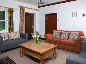 Ein Wohnzimmer mit grauem Sofa, orangefarbenem Sofa, Couchtisch aus Holz und einem Fenster mit Vorhängen.