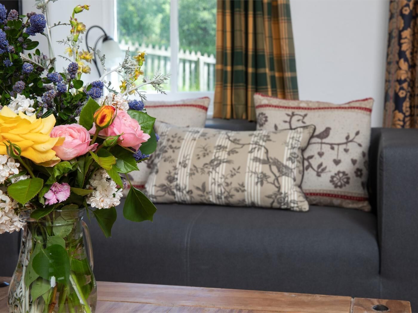 Een woonkamer met een bank, een decoratief kussen en een vaas met bloemen.