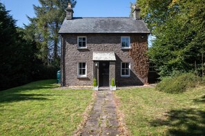 Ein Haus aus Stein mit einer zentralen Tür und zwei Fenstern im Obergeschoss.