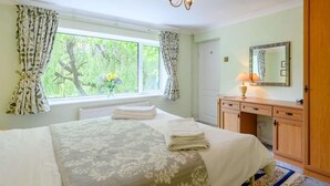 Ein Schlafzimmer mit Bett, einem Fenster mit Vorhängen, einem Nachttisch mit Lampe und einem Holzschrank.
