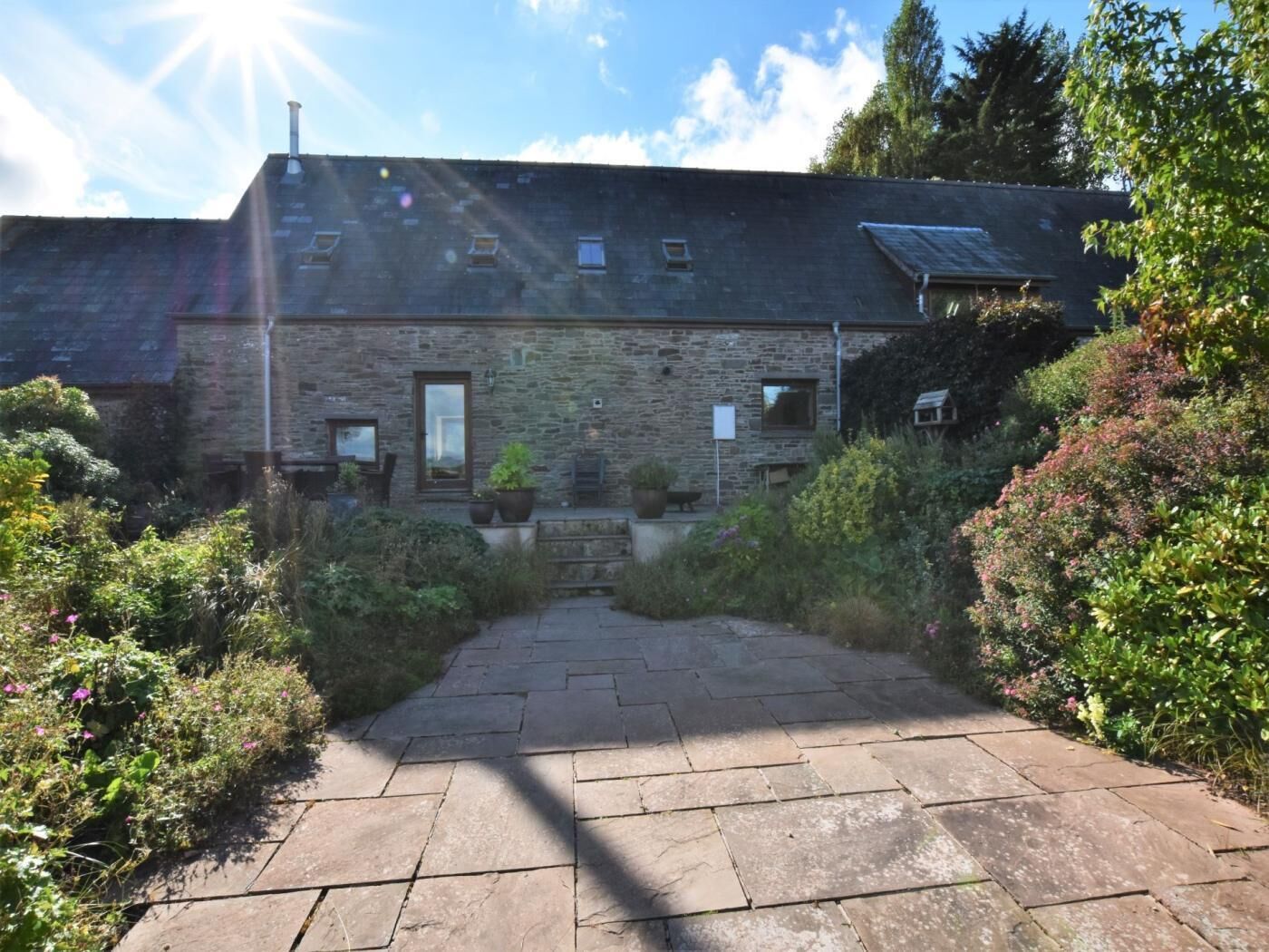 A stone building with a paved entrance, surrounded by greenery.