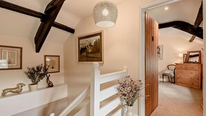 Eine Treppe mit weißen Geländern, einer hängenden Leuchte, gerahmten Bildern und einer Holzkommode in einer Diele.