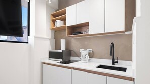 A modern kitchen with white cabinets, a black countertop, a coffee maker, and a sink. - Naya Sanctuary - Zenn (San Juan)