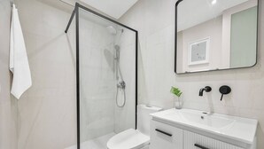 A modern bathroom with a glass-enclosed shower, a white toilet, a sink with a mirror, and a potted plant. - Naya Sanctuary - Zenn (San Juan)