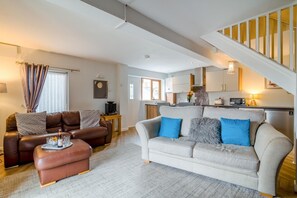 A living room with a sofa, ottoman, and a coffee table with drinks. There is a staircase leading to an upper level.