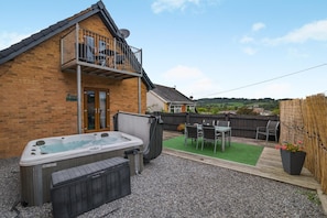 Ein Garten mit Whirlpool, einer Holzterrasse, einem Tisch mit Stühlen und Blick auf die Landschaft.