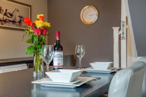 A dining table set with a bottle of wine, glasses, a vase with flowers, and a clock on the wall.
