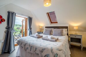 Ein Schlafzimmer mit einem Bett, zwei Nachttischen, einem Fenster mit Vorhängen und Blick ins Freie.