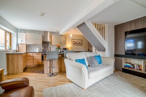 A modern living space with a kitchen, a sofa, a television, and a bookshelf.