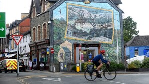 Ein Radfahrer fährt an einem Gebäude mit einem Wandbild einer Landschaft vorbei.