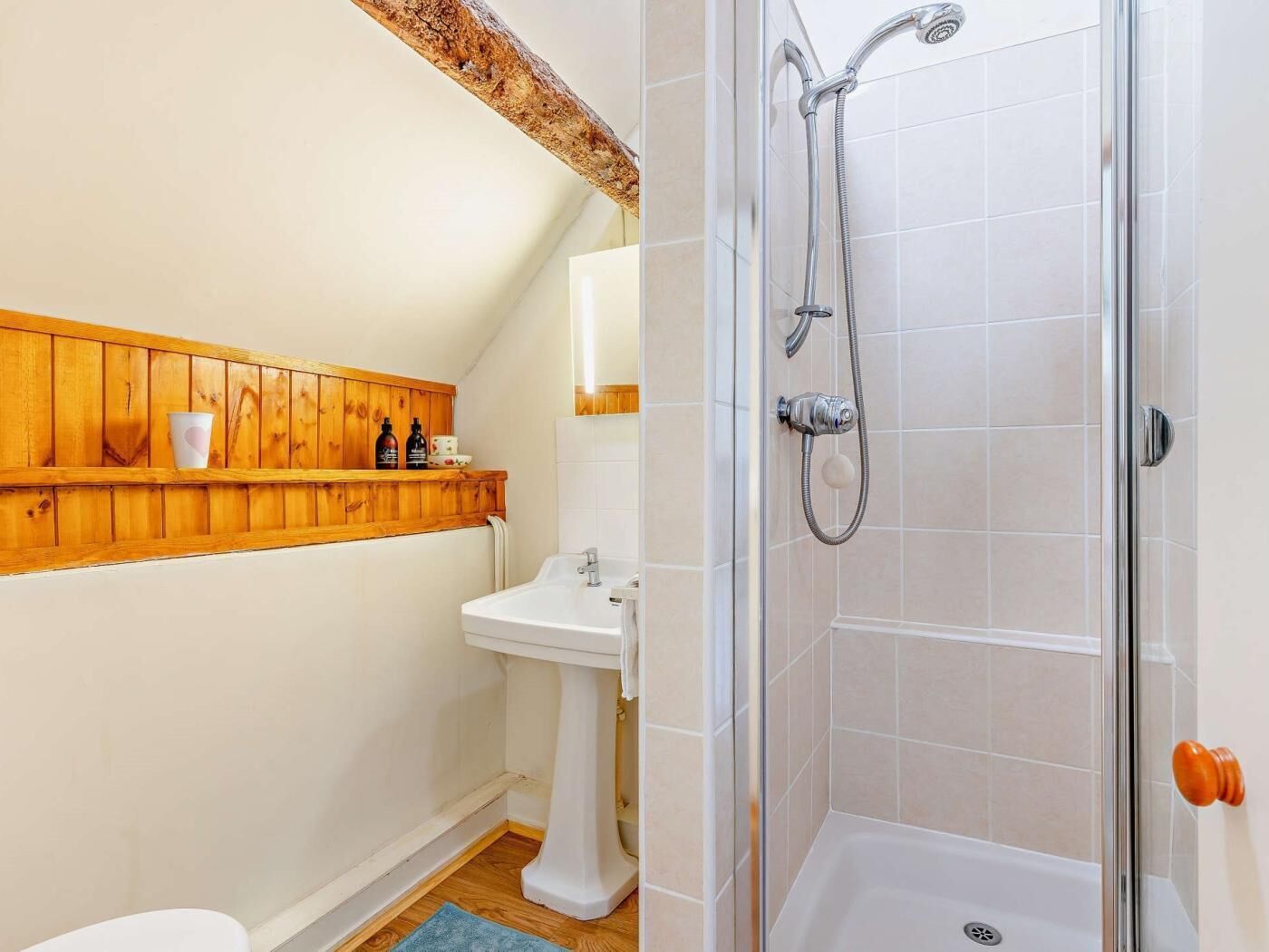 A bathroom with a wooden shelf, a pedestal sink, and a shower with a glass door.
