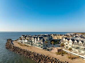 Un quartier résidentiel situé sur la côte, avec des immeubles à plusieurs étages, une digue rocheuse et une vue dégagée sur la mer.