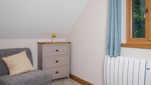 Ein Zimmer mit einer grauen Couch, einem Holzkasten mit Schubladen, einem Heizkörper und einem Fenster mit Vorhang.