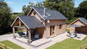 Een houten chalet met een overdekt terras, schoorsteen en een klein raam.
