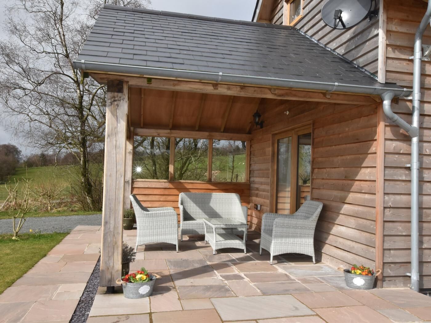 A wooden cabin with a covered patio, wicker furniture, and potted plants.