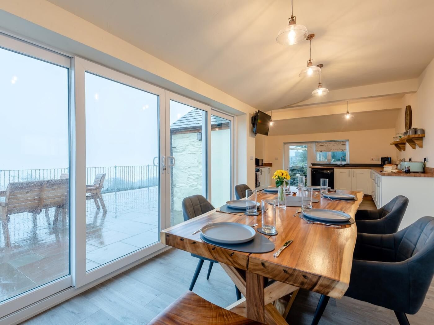 A dining area with a wooden table, chairs, and a view of the outdoors through large glass doors.