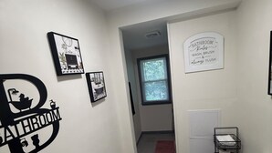 Ein Badezimmer mit Toilette, Waschbecken und Dusche. An den Wänden befinden sich Schilder und ein Fenster mit Jalousien.