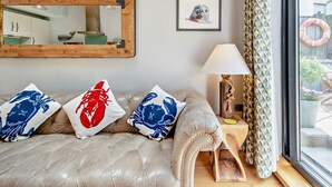 A room with a leather sofa, a wooden side table with a lamp, a framed picture, and a large mirror. - 2 Bed in Tenby (oc-fb001) (Tenby)