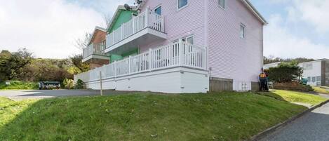 A multi-story residential building with a balcony, a driveway, and a grassy area.