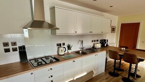 A modern kitchen with white cabinets, a gas stove, a sink, and bar stools. - 2 Bed in Tenby (oc-fb219) (Tenby)