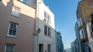 A narrow street lined with buildings, including a beige building with a door and windows, and a blue building with a door and windows.