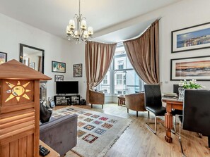 Ein modernes Wohnzimmer mit Fernseher, einer Holzdeko, einem gemusterten Teppich und einem Essbereich mit Stühlen und Tisch.