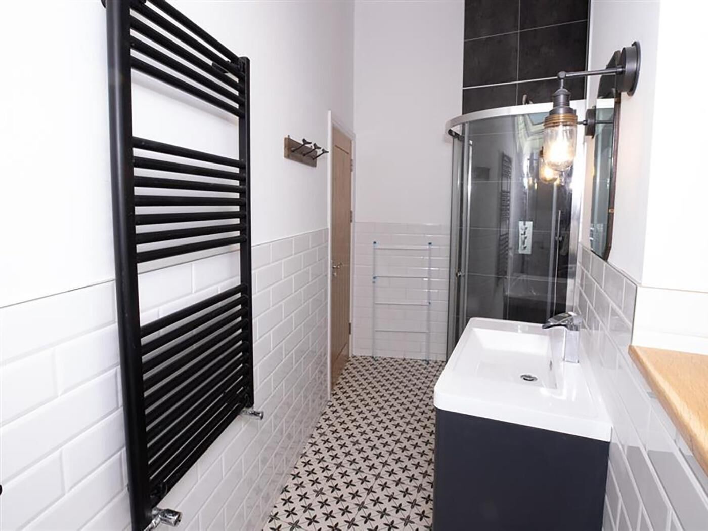 A bathroom with a black towel rack, a glass shower enclosure, and a white sink.
