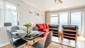 Ein modernes Wohnzimmer mit Essbereich, einem roten Sofa und Meerblick.