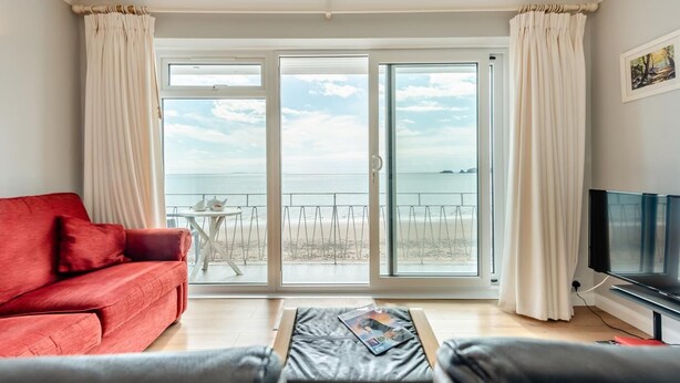 Ein Wohnzimmer mit einem roten Sofa, einem Flachbildfernseher und einem Balkon mit Meerblick.