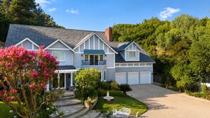 Ein zweigeschossiges Haus mit Garage, überdachter Veranda und einem gepflegten Garten mit Springbrunnen.
