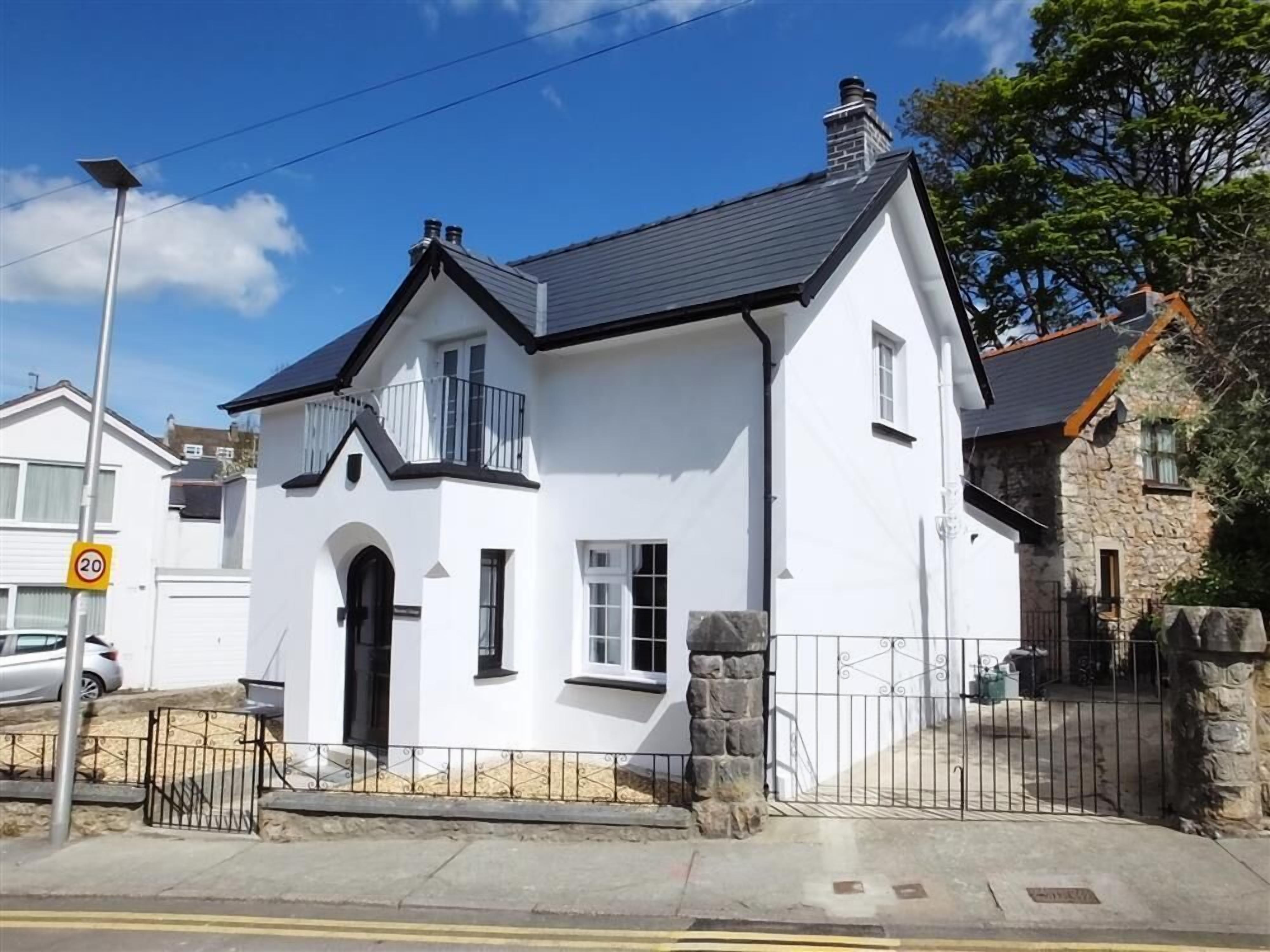 A white two-story house with a black roof, a stone wall, and a metal gate.