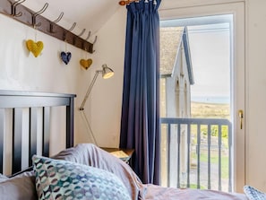 A bedroom with a bed, a nightstand, a lamp, a window with a view, and a curtain. - 3 Bed in Haverfordwest (oc-81072) (Mathry)