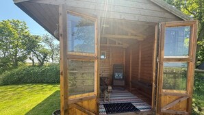 Eine Holzhütte mit geöffneten Türen, einem kleinen Innenraum und einem Garten davor.