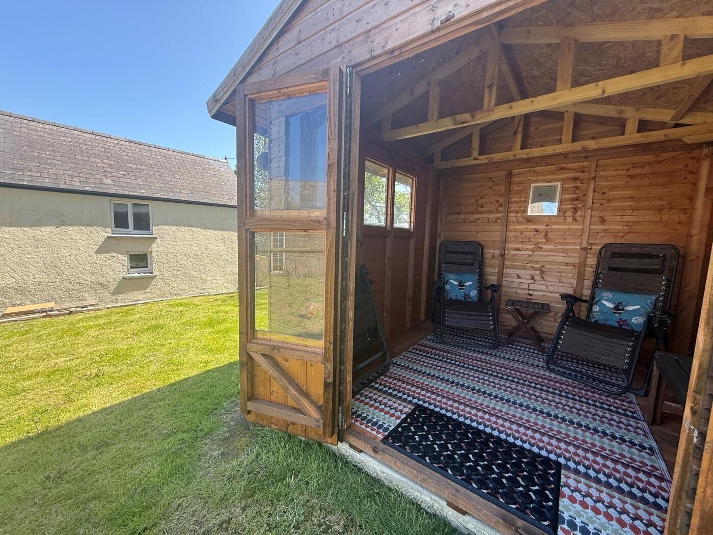 A wooden cabin with a porch, two reclining chairs, and a patterned rug.