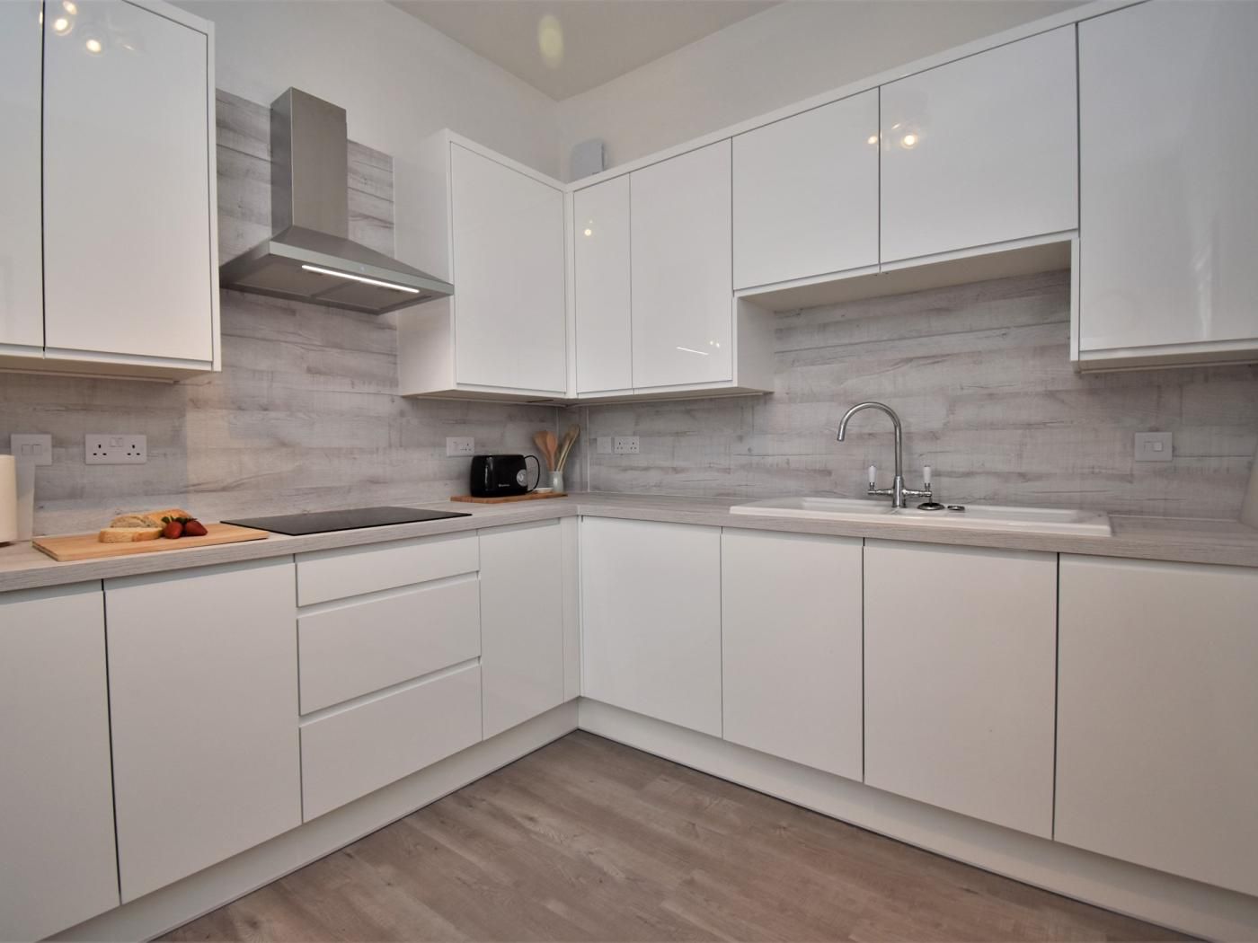 A modern kitchen with white cabinetry, a stainless steel range hood, a black microwave, and a wooden cutting board with fruit.