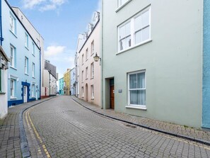 A cobblestone street lined with colorful buildings, a clear sky, and a quiet atmosphere. - 2 Bed in Tenby (oc-fb205) (Tenby)