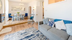 Un salón espacioso con un sofá gris, una zona de comedor con una mesa y sillas de madera, y una araña.